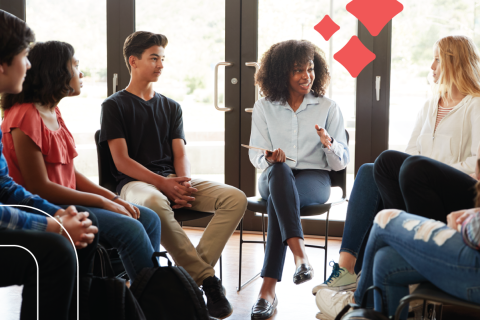 a group of teens sit around an adult as she explains a resource