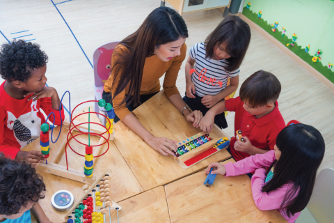 five kids aged 4–7 play with toys alongside their teacher 