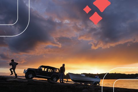 A man pulls a boat up from a boat ramp while a boy runs up the ramp. The pair are in front of a summer sunset