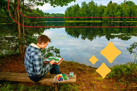young man sitting in front of scenic lake painting in a journal with watercolors